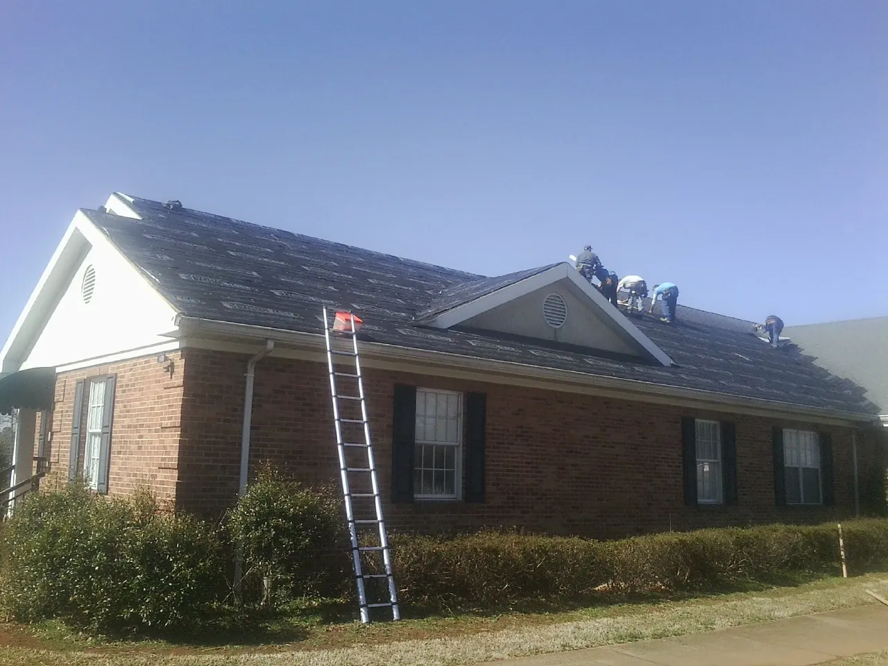 Crew tearing shingles off a brick ranch roof with a ladder set — Metal Roof Repair work by our crew in Villa Ridge