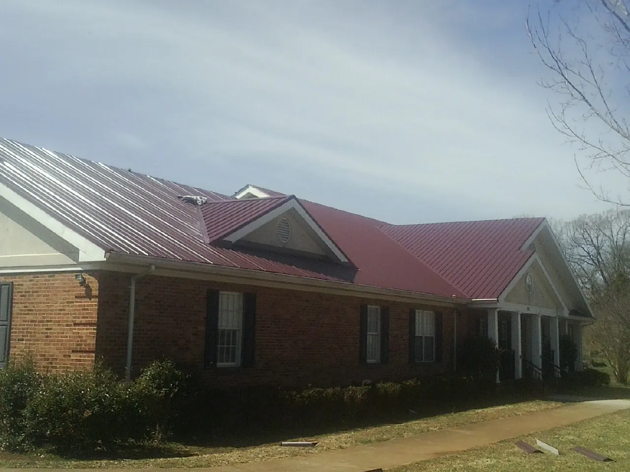 Red metal roof with gabled entries on a long brick building, from a Hail Damage Roof Repair job in Villa Ridge