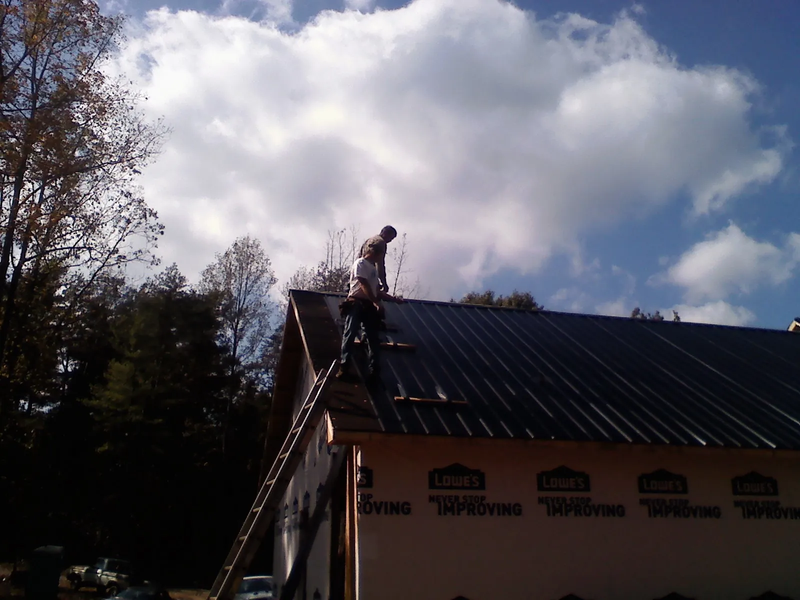 Roofer fastening dark metal panels high against a cloudy sky, from a Roof Inspection job in Villa Ridge