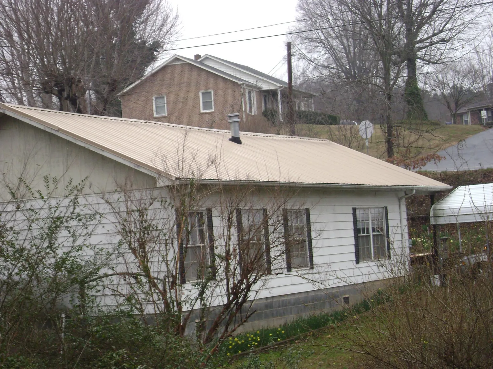 Tan metal roof on a white sided house set into a hillside — Commercial Roofing by Roofing Brothers in Villa Ridge