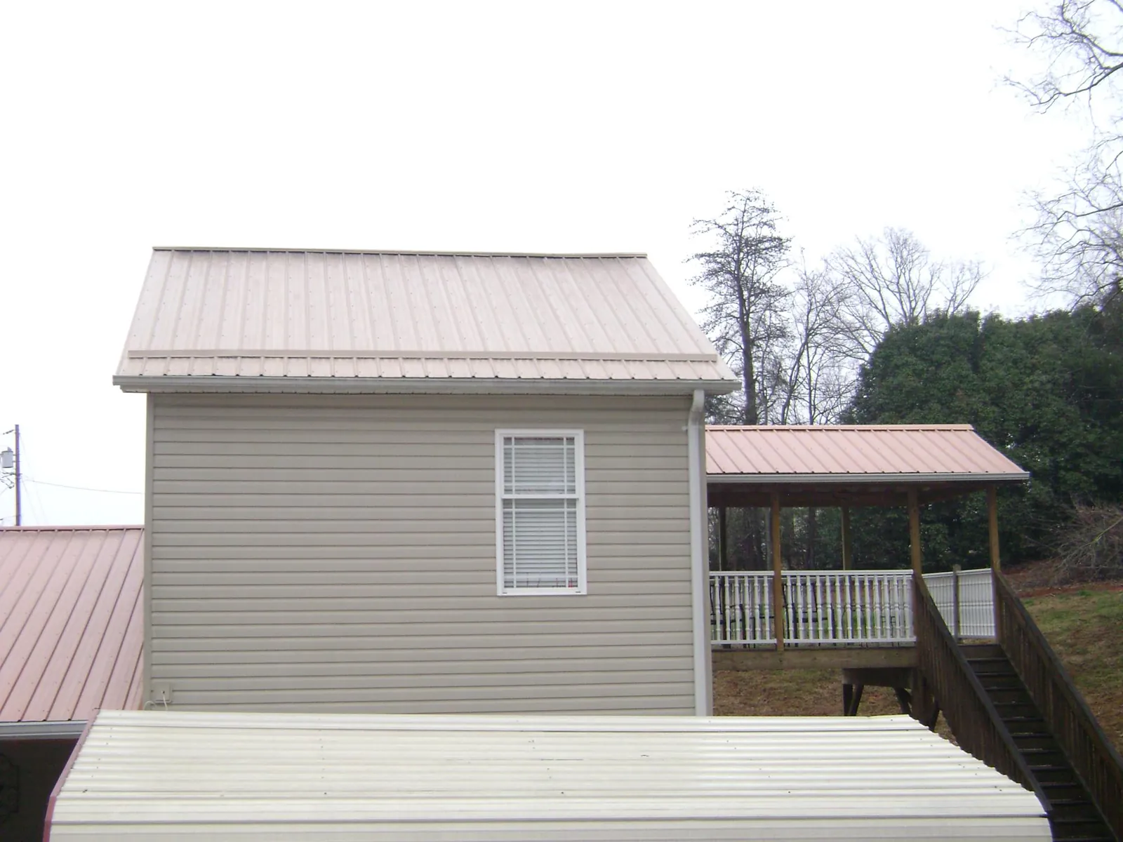 Tan metal roofs on a two story addition and attached porch, from a Roof Replacement job in Villa Ridge